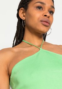 Top halter verde com nervuras e uma alça atada, apresentando um design ajustado que abraça suavemente o corpo. Textura suave com um acabamento ligeiramente brilhante.