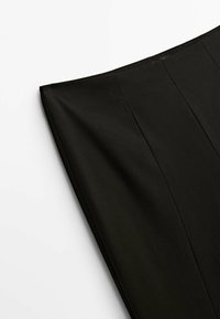 Gros plan sur une jupe crayon noire montrant un tissu lisse et des détails de coutures verticales sur fond blanc.