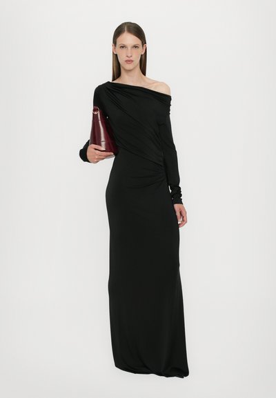 Black long-sleeve dress with a draped design and off-shoulder style. Model holds a burgundy handbag. Smooth fabric and form-fitting shape.