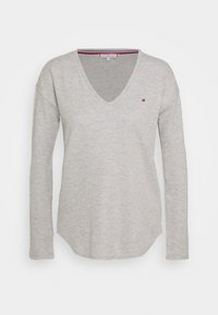 Lys grå langærmet V-hals sweater lavet af ribbet stof, med et lille logo på venstre bryst og en buet kant.