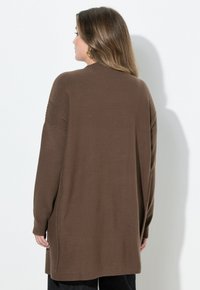 Brun långärmad cardigan i mjukt stickat tyg med ribbade detaljer på axlarna. Avslappnad passform, sidoflikar och medellång design.