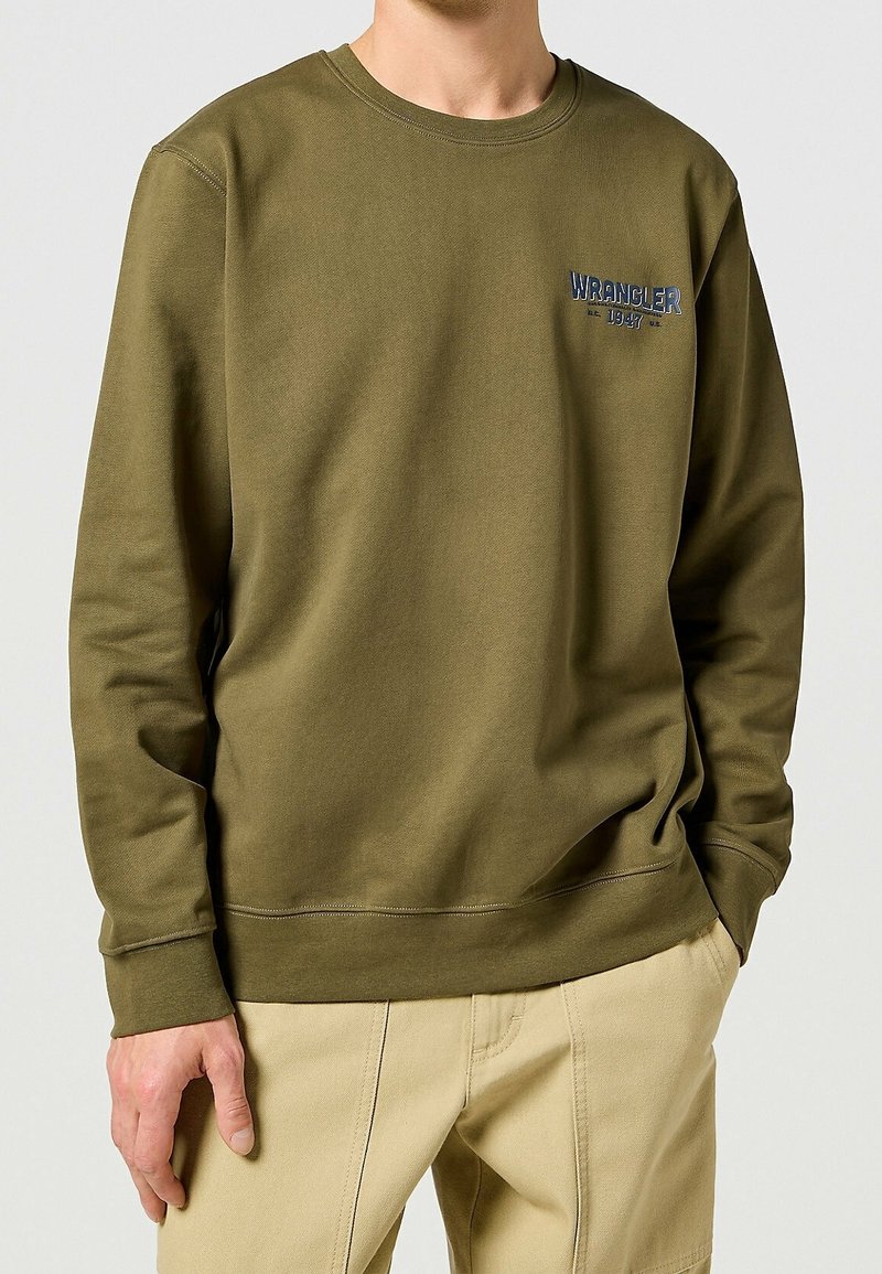Sweat-shirt vert olive à manches longues, col rond, avec un petit logo "Wrangler" sur la poitrine. Matière en coton doux avec une texture lisse.