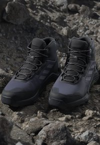 Pair of black high-top hiking boots with laces sitting on rough, rocky terrain.