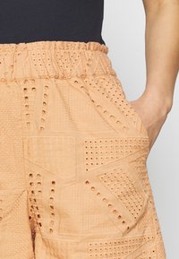 Shorts de couleur pêche en tissu texturé avec des motifs découpés, une taille élastique et des poches latérales.