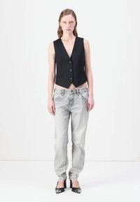 Gilet a righe nere con scollo a V e tre bottoni, abbinato a jeans grigi chiari e décolleté nere a punta.