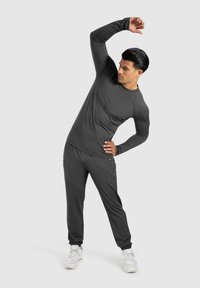 Dunkelgraues Sportoutfit mit langärmligem Oberteil und schmal zulaufenden Sweatpants, aus glattem Stoff gefertigt, mit elastischen Bündchen und einem elastischen Bund.