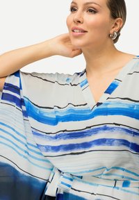 Kaftano a strisce blu con scollatura a V, maniche fluttuanti e una cintura in vita. Realizzato in materiale leggero con una finitura morbida e testurizzata.