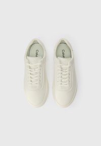 Bílé kožené tenisky se čtyřmi páry očí, plochými tkaničkami, polstrovaným límcem a logem na stélce. Hladký povrch a minimalistický design.