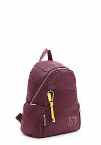 Sac à dos bordeaux en tissu texturé, avec des zips argentés, un accent jaune sur la tirette, et une poche latérale. Forme compacte et arrondie avec des sangles ajustables.