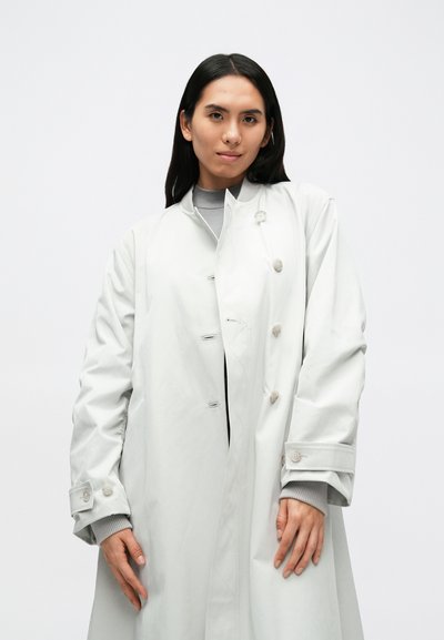 Világos szürke, hosszú ballonkabát sima textúrával, kör alakú gombokkal és mandzsetta részletekkel. Szürke belső réteggel van stílusosan kombinálva.
