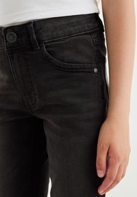 Čierne denimové džínsy so slim fit strihom, s prednými vreckami, diskrétnym prešívaním a okrúhlym kovovým gombíkom na zapínanie v páse.