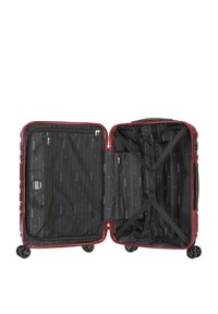 Valise rigide rouge avec un intérieur en tissu noir. Dispose de sangles élastiques, de poches zippées et de quatre roues pour plus de mobilité.