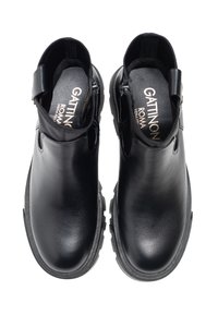 Botas de cuero negras hasta el tobillo con una textura suave, puntera redonda y suela de goma gruesa. Presentan un recorte lateral y un detalle de marca en el interior.