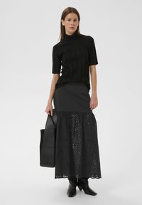 Schwarzes, geripptes Kurzarmoberteil mit hohem Ausschnitt, kombiniert mit einem langen schwarzen Rock mit lasergeschnittenen Mustern und einem ausgestellten Saum.