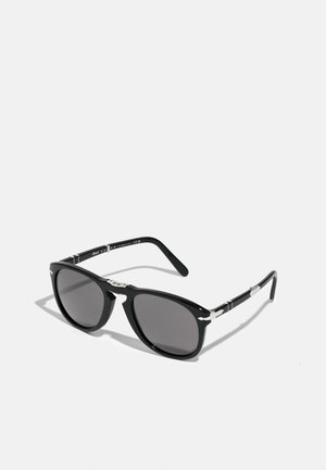 Occhiali da sole neri con montatura rettangolare in plastica e lenti scure. Accenti metallici in argento sulle aste, con un motivo testurizzato.