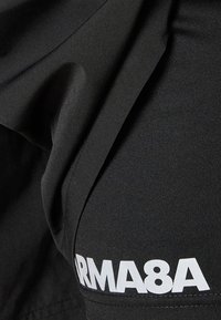 Schwarze Sportbekleidung aus Stoff mit glatter Textur, versehen mit dem weißen Logo-Text "ARMA8A" an der Seite. Das Design ist minimalistisch und modern.