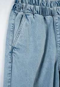 Jasnoniebieskie dżinsy z elastycznym pasem i sznurkiem do regulacji, z bocznymi kieszeniami i luźnym krojem. Widoczne detale szwów.