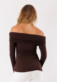 Top lungo marrone senza spalline con texture arricciata, design aderente e tessuto liscio. Nessun logo o motivo visibile.