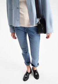 Light blue suede jacket, beige top, rolled-up light blue jeans, and black loafers. Small black crossbody bag with textured surface.
