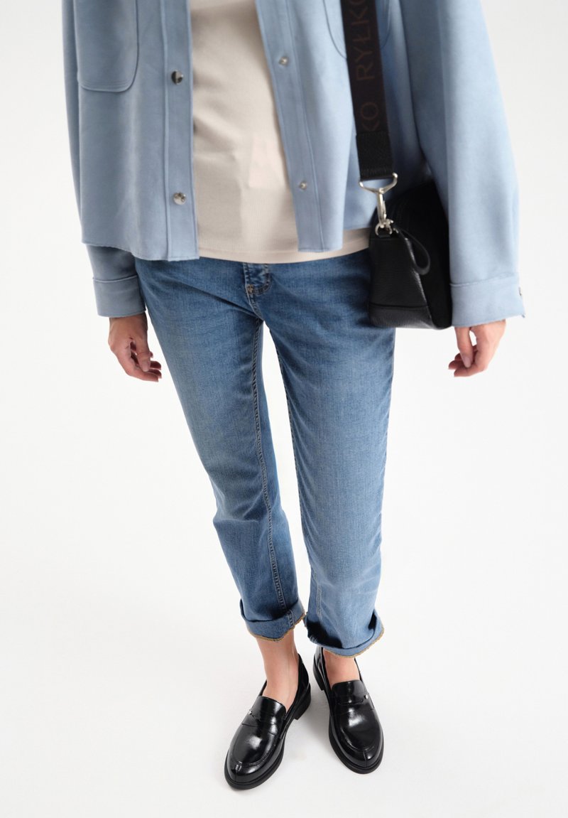 Light blue suede jacket, beige top, rolled-up light blue jeans, and black loafers. Small black crossbody bag with textured surface.