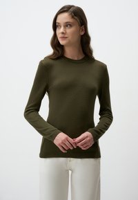 Maglione verde oliva a maniche lunghe con collo a girocollo a coste e superficie testurizzata. Indossato sopra pantaloni bianchi, evidenziando una silhouette aderente.
