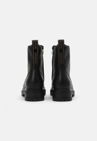 Bottes noires en cuir à la cheville avec une semelle épaisse, une fermeture éclair à l'arrière et une languette avec un motif de logo contrastant. Texture lisse et design épuré.