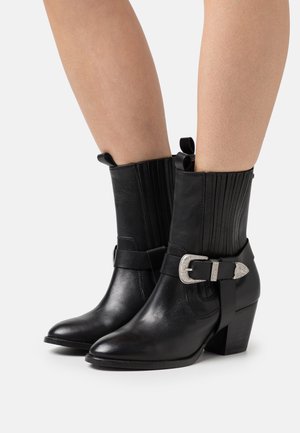 Sorte læder ankelstøvler med spidse tæer, teksturerede sidepaneler og en sølvspænde detalje på en rem omkring anklen.