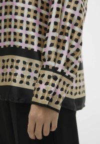 Blusa in seta con motivo geometrico in nero, beige e rosa. Maniche lunghe con polsino nero e dettaglio a bottone. Texture liscia.