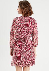 Robe à motif écossais rouge et blanc avec tissu transparent, manches trois-quarts et taille cintrée, présentant une jupe fluide.