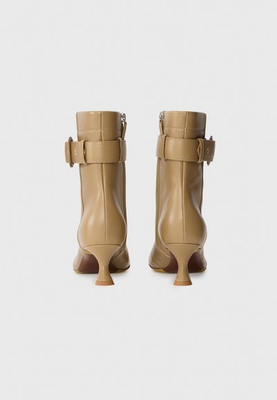 Bruna läderankleboots med en åtsittande skaft, en sidogzipper och ett brett vristband. Har en utsvängd klack och slät yta.
