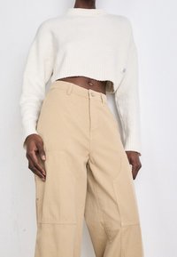 Cream cropped sweater with a ribbed neckline and cuffs, paired with beige wide-leg pants featuring side pockets and a button closure.