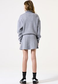 Grijze gebreide pullover met hoge kraag, gecombineerd met een geplooide grijze rok. Zwarte sokken met witte accenten en zwarte schoenen maken de outfit compleet.