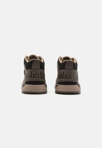 Botas de ante marrón hasta el tobillo con un interior de tejido beige, que presentan un logotipo embosado prominente en el talón y una suela acolchada para mayor comodidad.