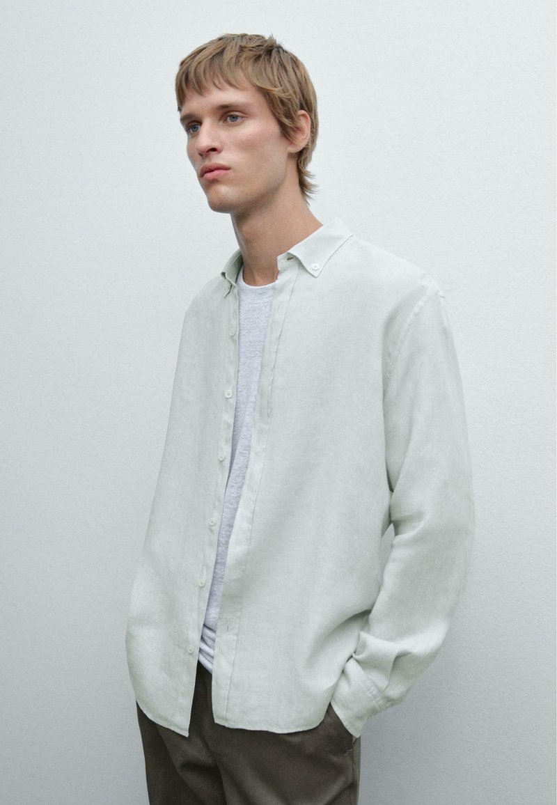 Chemise vert clair à boutons en tissu doux et texturé, avec un col évasé et une coupe décontractée, superposée à un t-shirt gris.