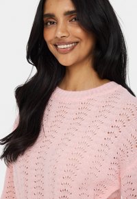 Light pink knitted sweater featuring an openwork pattern, round neckline, and long sleeves, showcasing a soft texture.