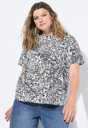 Top de manga corta con estampado paisley en blanco y negro, de corte holgado, hecho de una tela con una textura suave. Combinado con vaqueros azules.