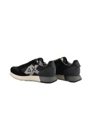 Sneaker neri e grigi caratterizzati da un mix di materiali in suede e mesh, con un design del logo distintivo e una suola in gomma testurizzata.