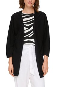 Schwarzer Cardigan mit offenem Front, lockerer Passform, 3/4-langen Ärmeln, aus strukturiertem Material. Kombiniert mit einem gestreiften schwarz-weißen Oberteil und weißen Hosen.