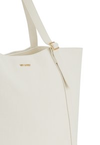 Sac en toile de couleur écrue, présentant une forme structurée, des accents en métal doré et un détail de fermeture éclair sur un côté.