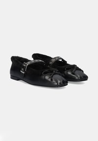 Mocasines de cuero negro con un suave forro de piel negra, con una correa decorativa con tachuelas plateadas y un lazo en la puntera.