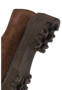Brown suede boot heel with layered black sole featuring deep, rugged treads for enhanced grip and durability.