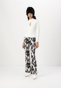 White long-sleeve top with a keyhole cutout, paired with black-and-white spotted flared pants and white heeled ankle boots. Black fur hat.