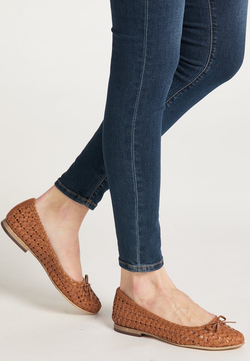Bruine geweven ballerina's met een ronde neus en strik, gecombineerd met donkerblauwe skinny jeans, die een comfortabele casual uitstraling benadrukken.