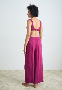 Magenta two-piece outfit featuring a textured crop top with wide straps and high-waisted, loose-fitting pants with an elastic waistband.