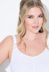Il top bianco senza maniche presenta un collo a giro e spalline. Il tessuto appare liscio, con una silhouette aderente e dettagli di cucitura minimi.