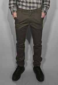 Pantaloni cargo verde scuro a taglio slim, con tasche anteriori e una tasca cargo laterale, abbinati a scarpe sportive nere.