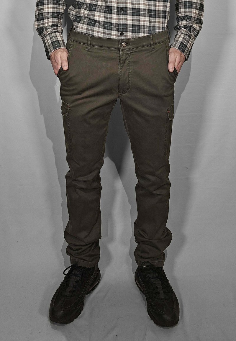 Pantaloni cargo verde scuro a taglio slim, con tasche anteriori e una tasca cargo laterale, abbinati a scarpe sportive nere.