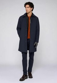 Marinblå kappa med rak skärning, matchande marinblå byxor, orange skjorta och mörka handskar; slät textur med knäppningsdetaljer.