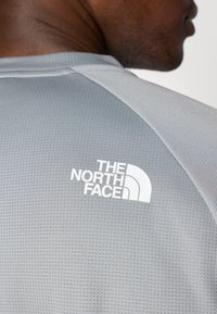 Gray short-sleeve shirt with a textured fabric, featuring a white logo "The North Face" on the upper back near the shoulder seam.