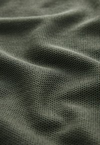 Mörkgrön, texturerad tyg med ett bikakesmönster, som visar lätt drapering och varierande yttension.